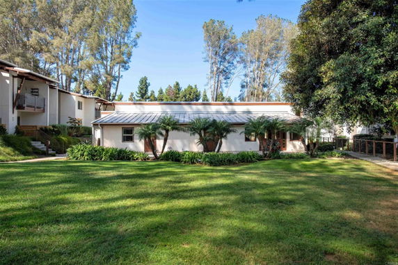 Front view of a single-story building with a flat roof surrounded by trees and greenery.