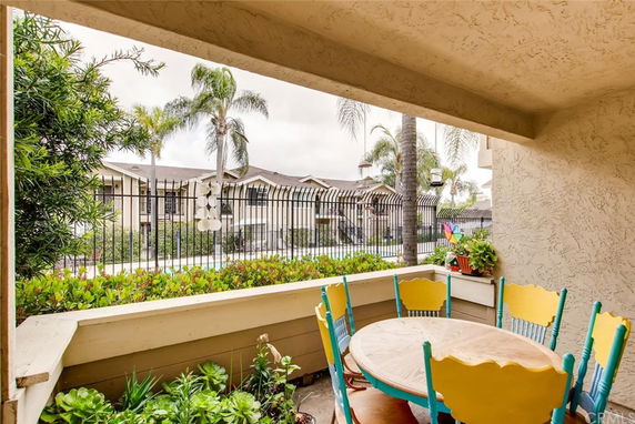Patio view looking out to apartment buildings surrounded by greenery and palm trees.