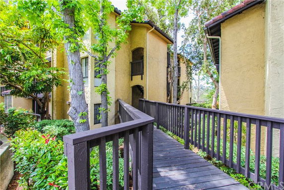 Front view of a multi-story building with a wooden walkway and surrounded by trees.