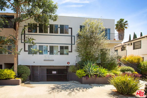 Front view of a two-story building with a gated entrance and surrounding plants.