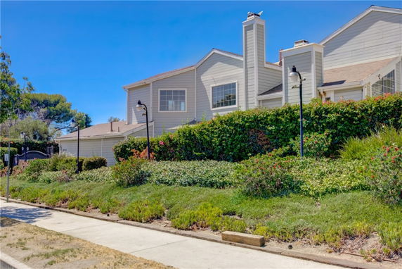 Front view of a two-story house with chimneys and a hedge-lined sidewalk.