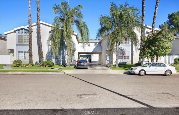 Front view of a two-story house with a driveway and palm trees.