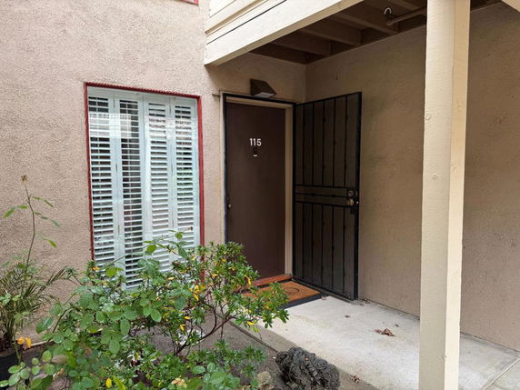 Exterior view of an entrance to an apartment with a door numbered 115 and a window with shutters.