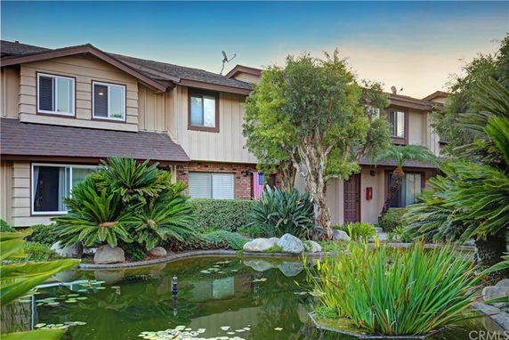 Front view of a two-story house with wooden siding and a pond with lush greenery.
