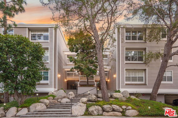 Front view of a multi-story residential building with large windows and surrounding trees.
