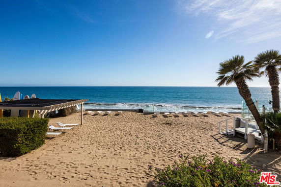 View from a beach showing the ocean and sandy shore with loungers.
