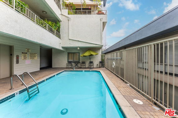 Outdoor swimming pool in an apartment complex with seating area and railing.