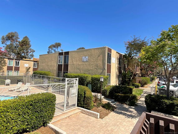View of an apartment complex with a fenced area and surrounding greenery.