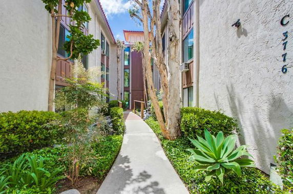 Front view of a multi-story residential building with a walkway and lush greenery.