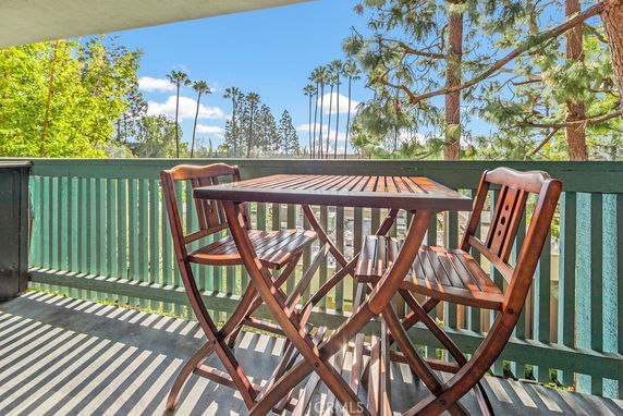Balcony with wooden table and chairs overlooking a view of trees and a clear blue sky.