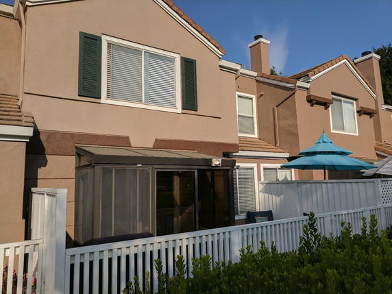 Front view of a two-story house with shuttered windows and a fenced patio area.