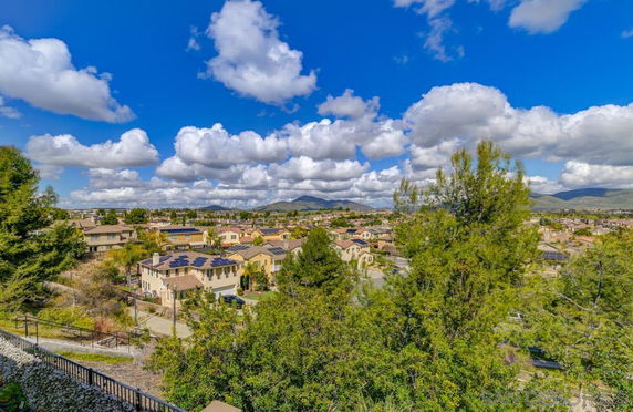 Wide angle view of a residential area with multiple houses, trees, and a partly cloudy sky in the background.