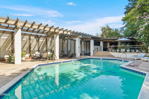 Outdoor area with a swimming pool and seating under a pergola.
