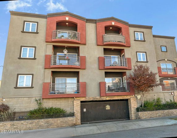 Front view of a multi-story apartment building with balconies and a gated parking entrance.