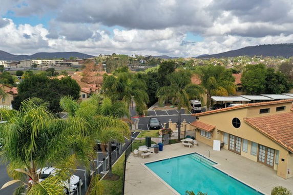 Aerial view of a swimming pool and surrounding residential area with palm trees and distant hills.