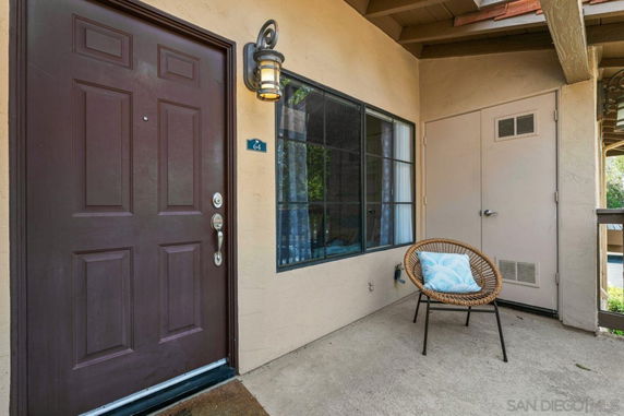 Front view of an entryway with a brown door and a window next to a chair.