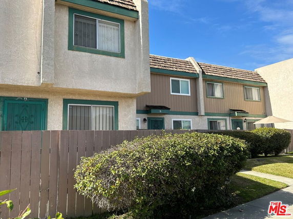 Front view of a multi-story townhouse with a shingled roof and fenced area.