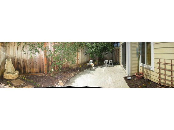 Panoramic view of a small backyard with a wooden fence and patio area.