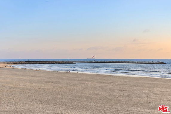 Wide view of a sandy beach with a jetty and calm sea.