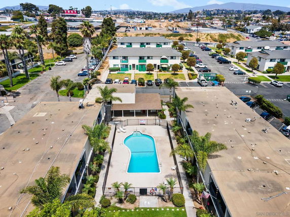 Aerial view of a residential complex with a central swimming pool, surrounded by buildings and parking areas.