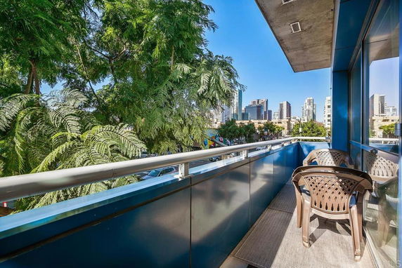 View from a balcony with two chairs overlooking a cityscape with trees and buildings.