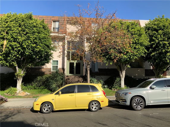 Front view of a multi-story building with a tiled roof, surrounded by trees and parked cars.