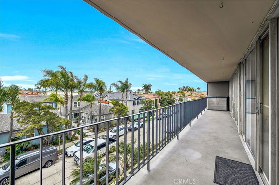 Balcony view overlooking residential area with palm trees and parked cars.
