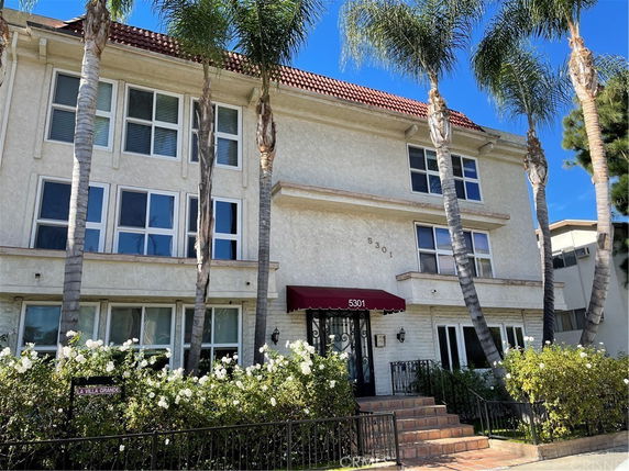 Front view of a multi-story building with red awnings and large windows.