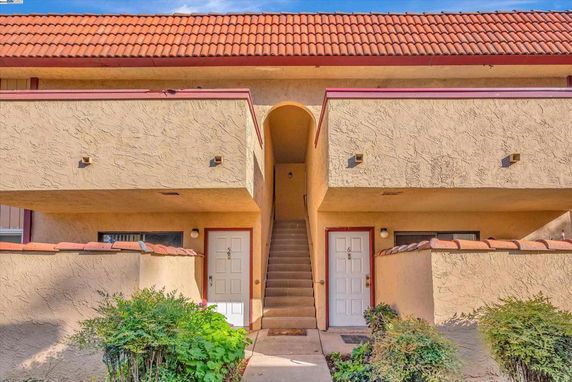 Front view of a two-story building with stucco walls and red-tiled roof, featuring two doors and an external staircase.