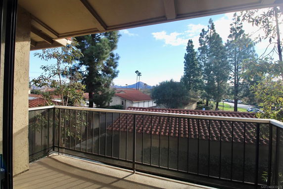 View from a balcony overlooking rooftops and trees with mountains in the background.