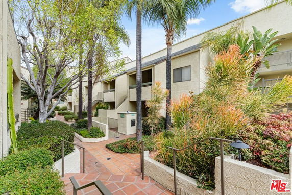 View of a building with a walkway lined with plants and trees.