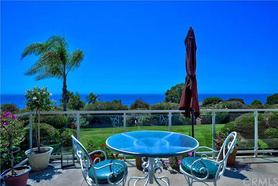 Outdoor patio with a round table and chairs overlooking a garden and ocean view.