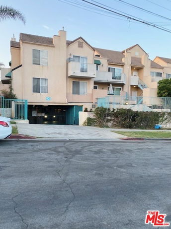 Front view of a multi-story residential building with balconies and a gated parking entrance.