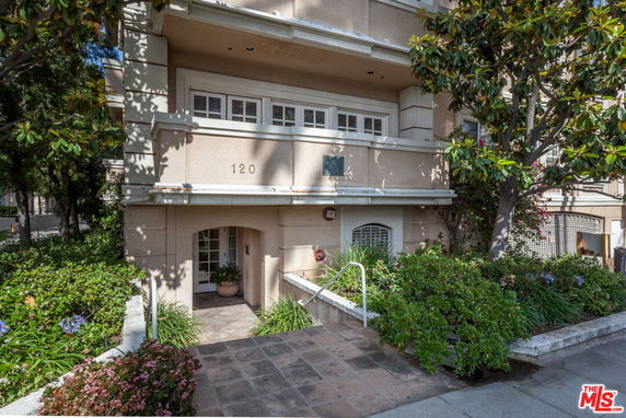 Front view of a multi-story building with a small entranceway and surrounding plants.