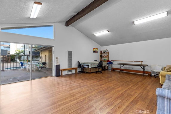 Spacious room with wooden flooring, tables, chairs, and a view of a swimming pool through glass doors.