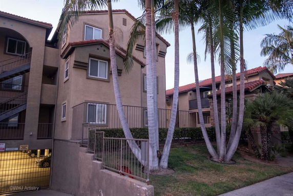 Front view of a multi-story apartment building with palm trees and a gated parking area.