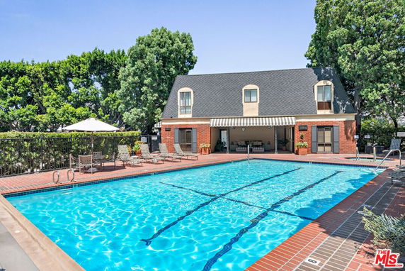 Outdoor swimming pool adjacent to a building with a sloped roof and brick facade.