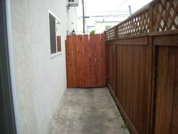 Narrow outdoor path beside a building with a wooden fence.