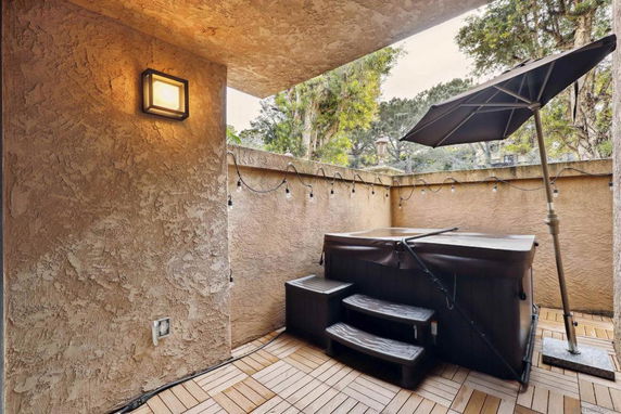 Small patio area with a hot tub and umbrella, surrounded by walls and string lights.