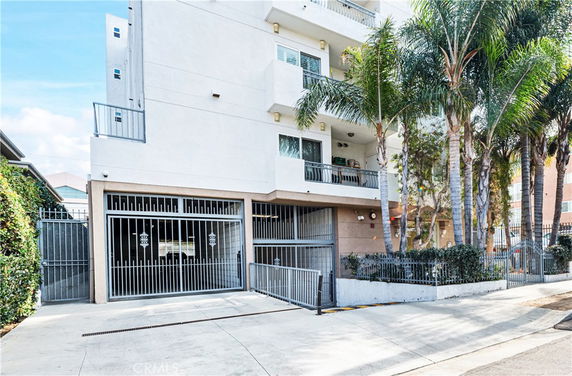 Front view of a multi-story building with balconies and gated parking entrance