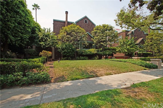 Front view of a multi-story house with brown shingles and a chimney, surrounded by trees and greenery.