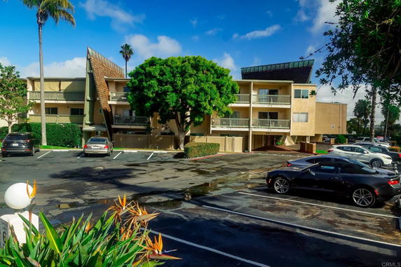 Outdoor parking area in front of a multi-story building with balconies.