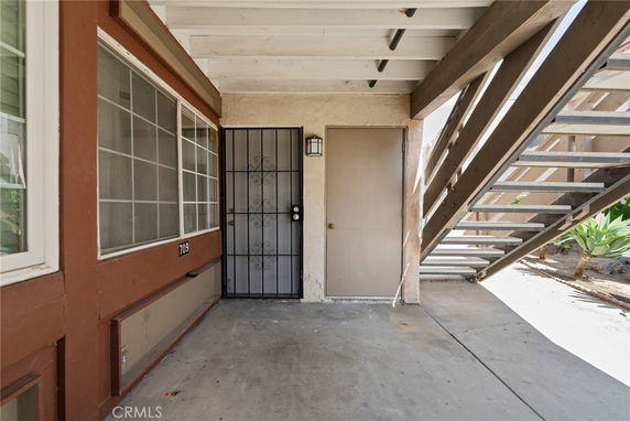 Front view of a residential unit with metal security door and adjacent window under a staircase.