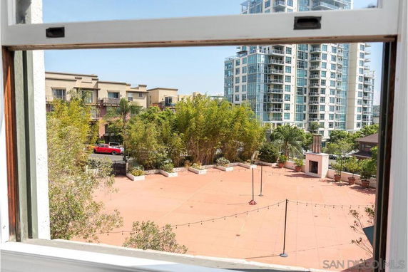 View from a window showing a patio area with buildings and greenery in the background.