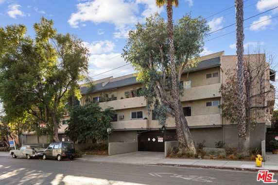 Front view of a multi-story apartment building with trees and parked cars.