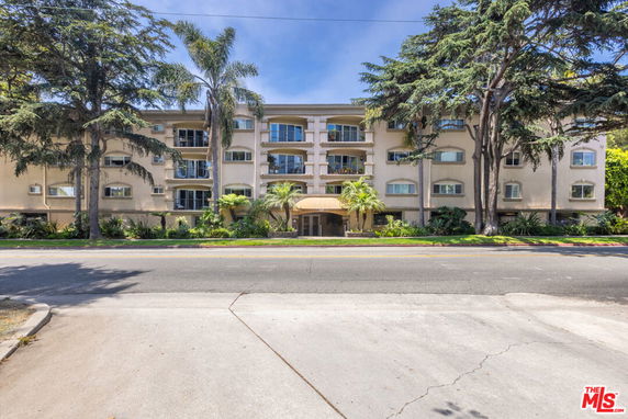 Front view of a multi-story apartment building with balconies and surrounded by trees.