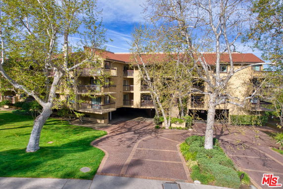 Front view of a multi-story residential building with balconies and a paved driveway.