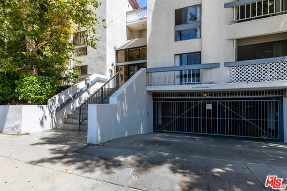 Front view of a residential building with a stairway entrance and gated parking area.