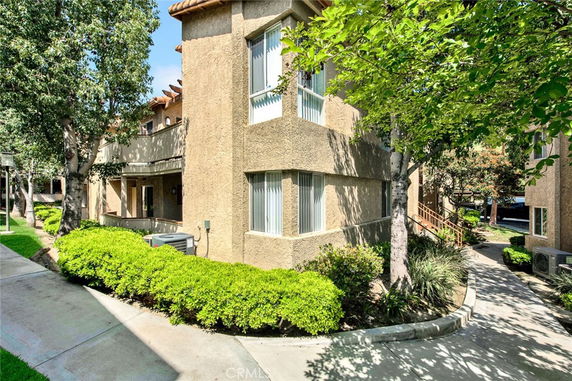 Front view of a multi-story residential building with beige stucco exterior and surrounding greenery.