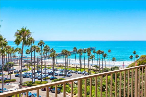 Panoramic view of palm trees, beach, pier, and ocean from a building.